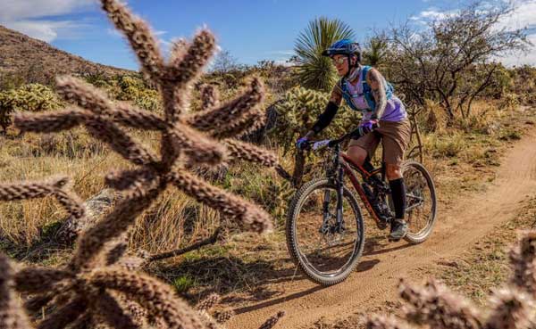 Female mountain biker riding trail through arid cactus landscape